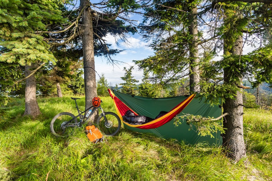 Camping in woods with hammock and sleeping bag on mountain biking adventure trip in green mountains. Travel campsite when mtb cycling with backpack. Lightweight shelter in wilderness forest, Poland.