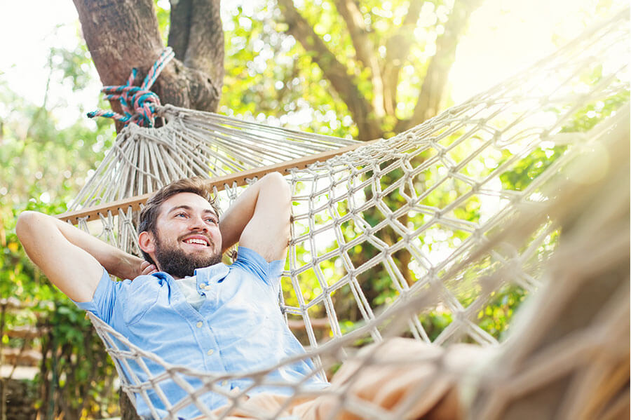 A smiling man enjoying and relaxing in his hammock outdoors.