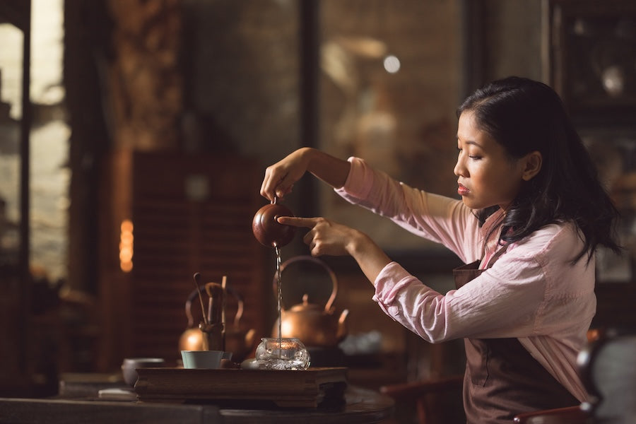 a young eastern woman pouring tea, using a traditional tea set