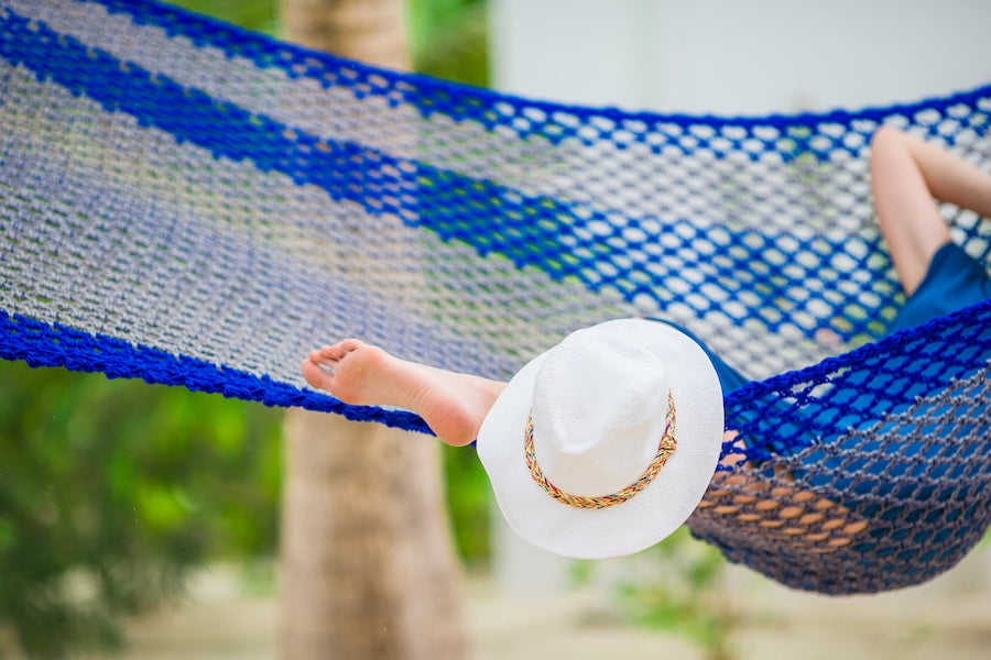 Closeup straw beach hat near relaxing young woman/ Woman relaxing on hammock on tropical vacation