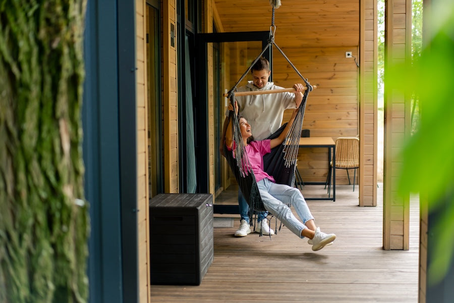 two young people on a deck, the woman in a hammock chair, the man behind her, laughing