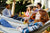 Hammock party concept - a woman with a drink in her hand, lying on a hammock outdoors, in blurred backround there are other people in hammocks, drinking and talking among themselves